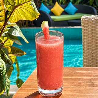 A tall glass of watermelon juice on a table beside the pool at Amber Poolside.