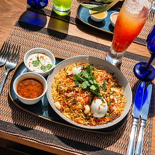 Biryani at Amber Poolside with raita and curry sauce, a cold drink alongside.