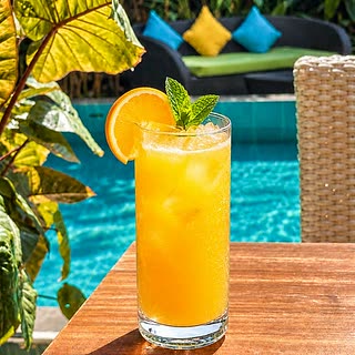 A tall glass of orange juice on a table beside the pool at Amber Poolside.