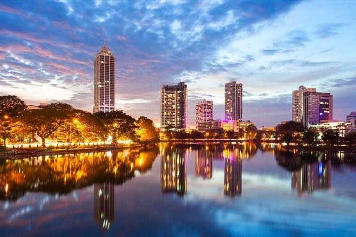 Colombo’s towers reflected in still water at dusk, the sky streaked pink and blue.