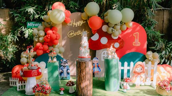 A first birthday set up at Amber Poolside, balloons and a red and green toadstool display among the greenery.