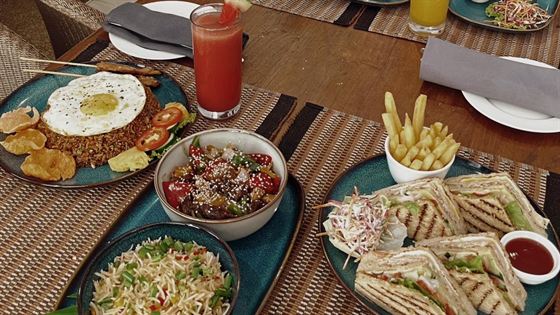 A breakfast spread at Amber Poolside, rice, curries, eggs and fresh juice on a timber table.