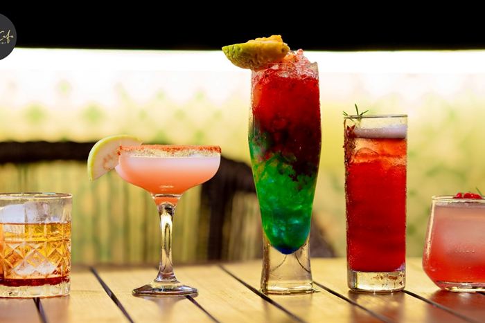 Four cocktails in a row on a timber bar at Cloud Café & Bar, pink, green and amber against a bright backdrop.