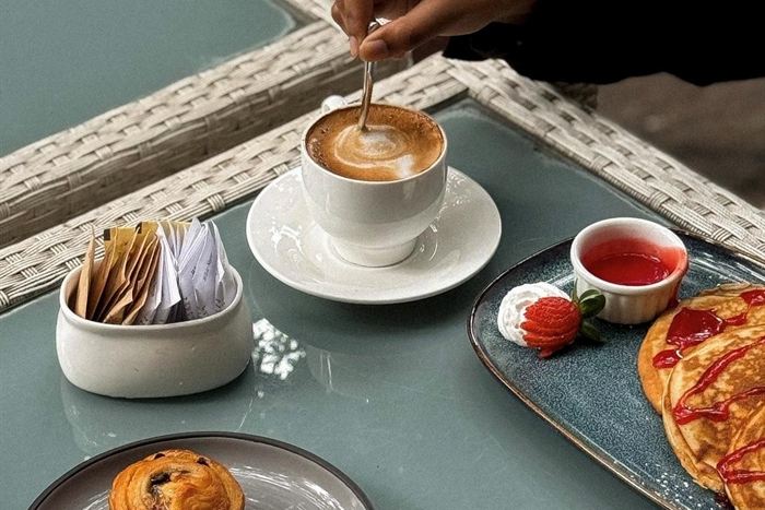 A coffee being stirred beside a plate of pastries on a cane tray at Colombo Court.