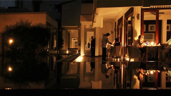 The poolside at Colombo Court in darkness, candles lit along the edge of the water and reflected in it.