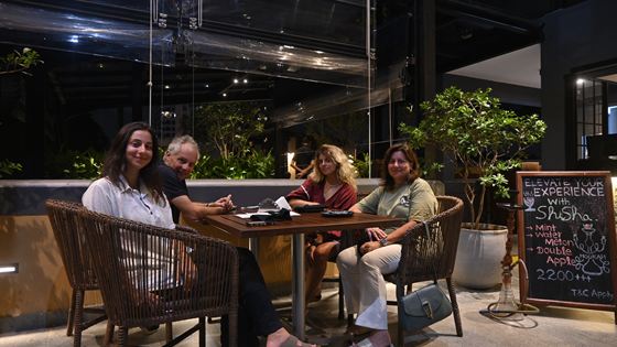 A table of people eating outdoors at Colombo Court after dark, lamps lit and a menu board behind them.