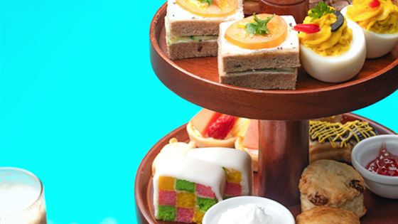 An English high tea stand at Amber Poolside, three tiers of sandwiches, scones and small cakes beside the turquoise pool.