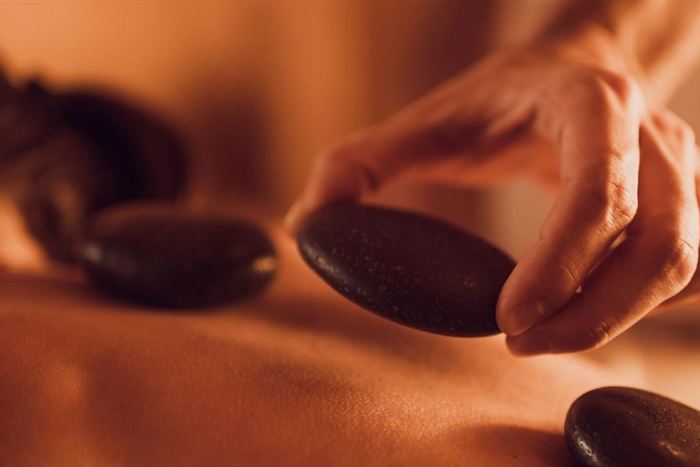 A therapist&rsquo;s hands placing dark heated stones on a guest&rsquo;s back during a hot stone massage.