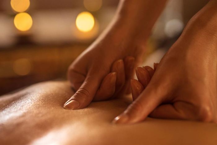 A therapist’s hands pressing along a guest’s back during a massage, warm light behind.
