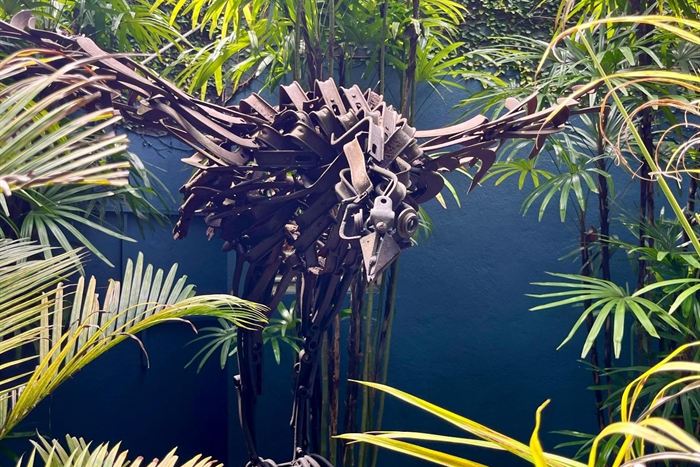 Palm fronds sculpted from scrap metal against a dark wall at Colombo Court, real palms in front.