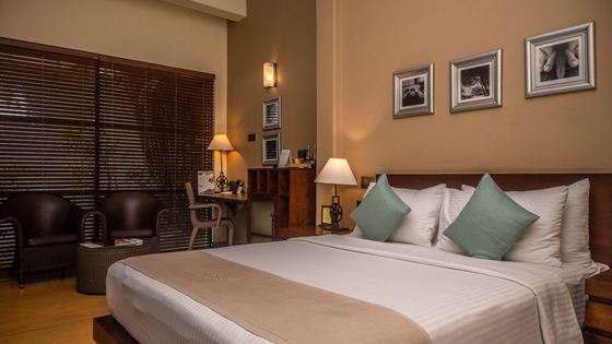 A bed made up in a room at Colombo Court, framed prints above it and blinds at the window.