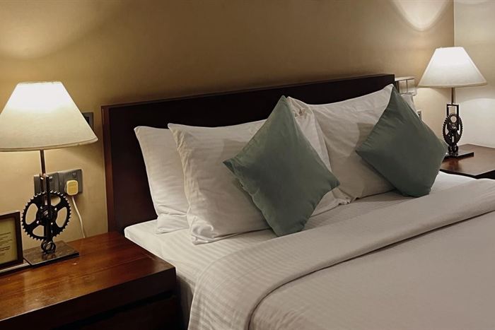 A bed at Colombo Court with grey and white cushions, bicycle-part bedside lamps lit on either side.
