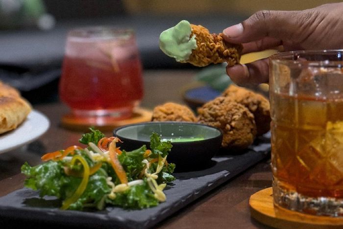 Small plates and two cocktails on a dark table at Cloud Caf&eacute; & Bar, fried bites and a salad.