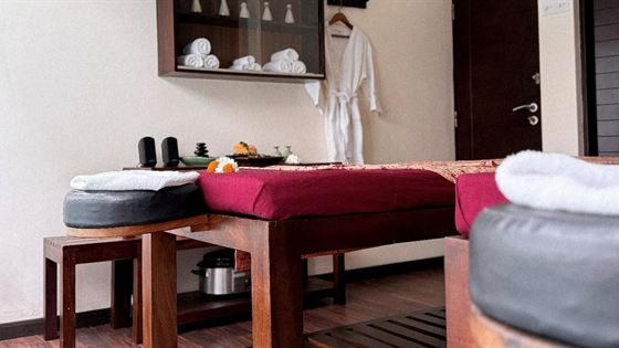 A treatment room at The Court Spa, a red-covered massage bed with rolled towels and a robe hanging beside it.