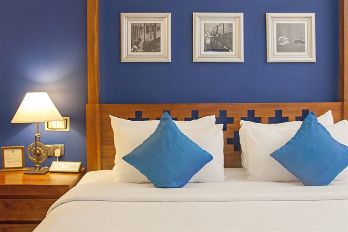 The bed in the Luxury Honeymoon Suite, blue cushions on white linen beneath framed photographs.