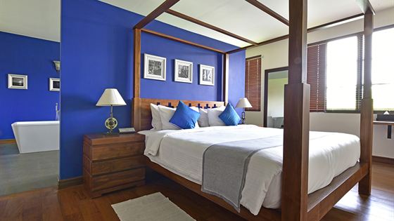 The Luxury Honeymoon Suite at Colombo Court, a four-poster bed against a deep blue wall with the bath beyond.