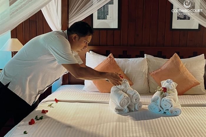 A housekeeper arranging towel animals and rose petals on a white bed beneath a canopy.