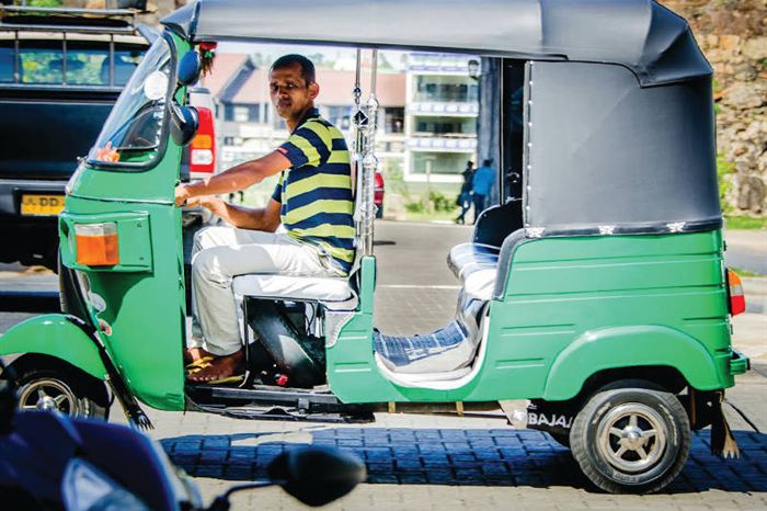 A green three-wheeler tuk-tuk on a Colombo street, its driver looking back at the camera.