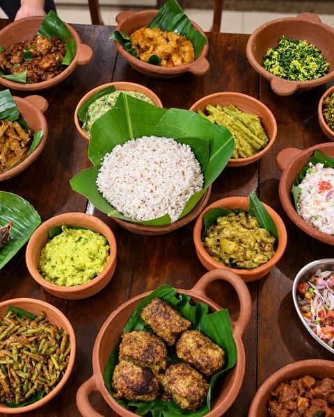 A Sri Lankan rice and curry spread in clay bowls on a timber table, rice on a banana leaf in the middle.