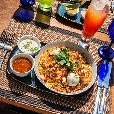 Biryani at Amber Poolside with a boiled egg, raita and curry sauce, a cold drink alongside.