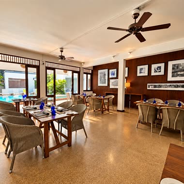 The dining room beside Amber Poolside, cane chairs at timber tables and the pool beyond the doors.