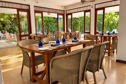 A table laid with blue glassware in the dining room beside Amber Poolside, the pool through the open doors.