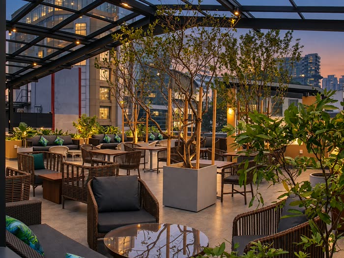 The Cloud Café & Bar rooftop at dusk, planted beds and cane seating under its glass roof with the towers of Colombo 3 beyond.