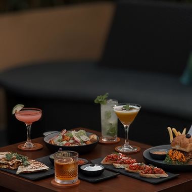 Cocktails and small plates across a dark timber table at Cloud Café & Bar.