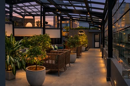 Low cane seating along the rooftop at Cloud Café & Bar, plants in white pots and warm light along the floor.