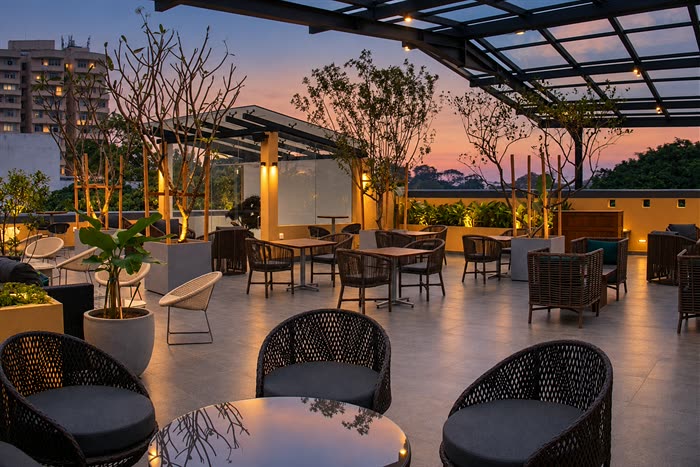 The rooftop at Cloud Caf&eacute; & Bar at dusk, planted beds and cane seating under the glass roof with the city sky turning pink.