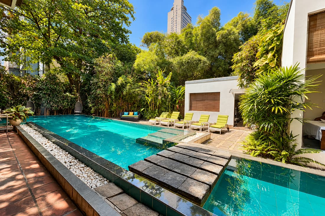 The pool at Colombo Court by day, loungers and dense planting on both sides with the city beyond the trees.