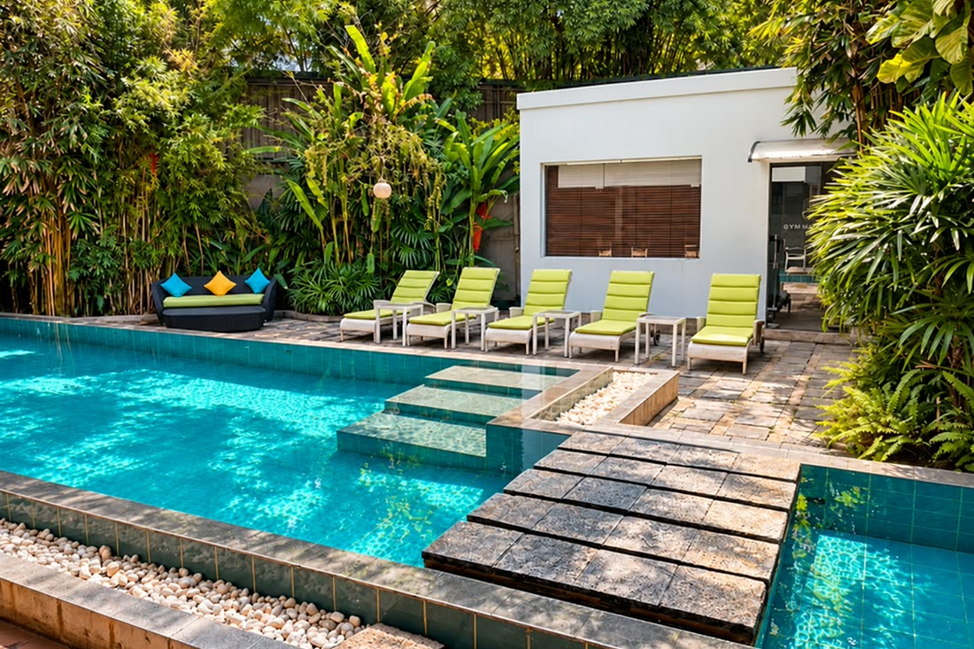 The pool at Colombo Court in daylight, stepping stones across the water and green loungers beyond.