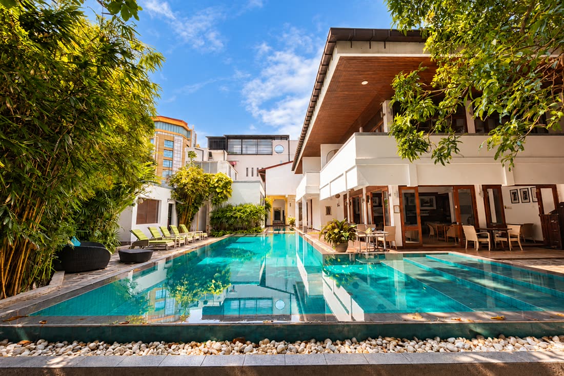 The pool at Colombo Court running the length of the garden on a bright day, white walls and bamboo either side.