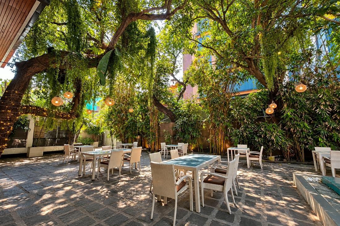 Tables set under the old tree in the garden at Colombo Court, dappled light across the stone floor.