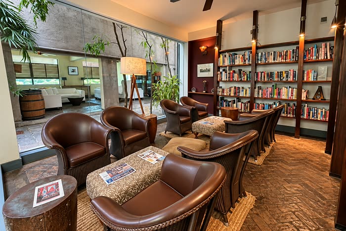 The library at Colombo Court, leather armchairs beside a wall of books with the garden through the glass.