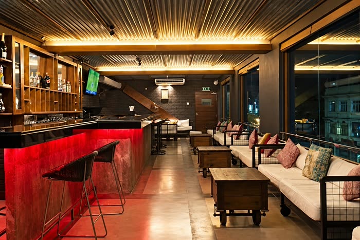 The Loft bar and lounge at Colombo Court, a lit red counter with stools and low sofas by the window at night.