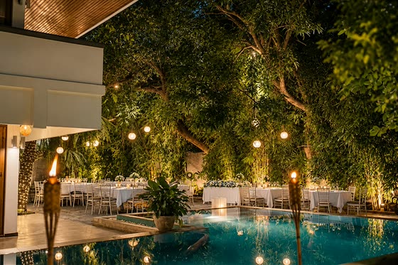 The poolside garden at Colombo Court after dark, lanterns in the trees and tables laid beside the lit pool.