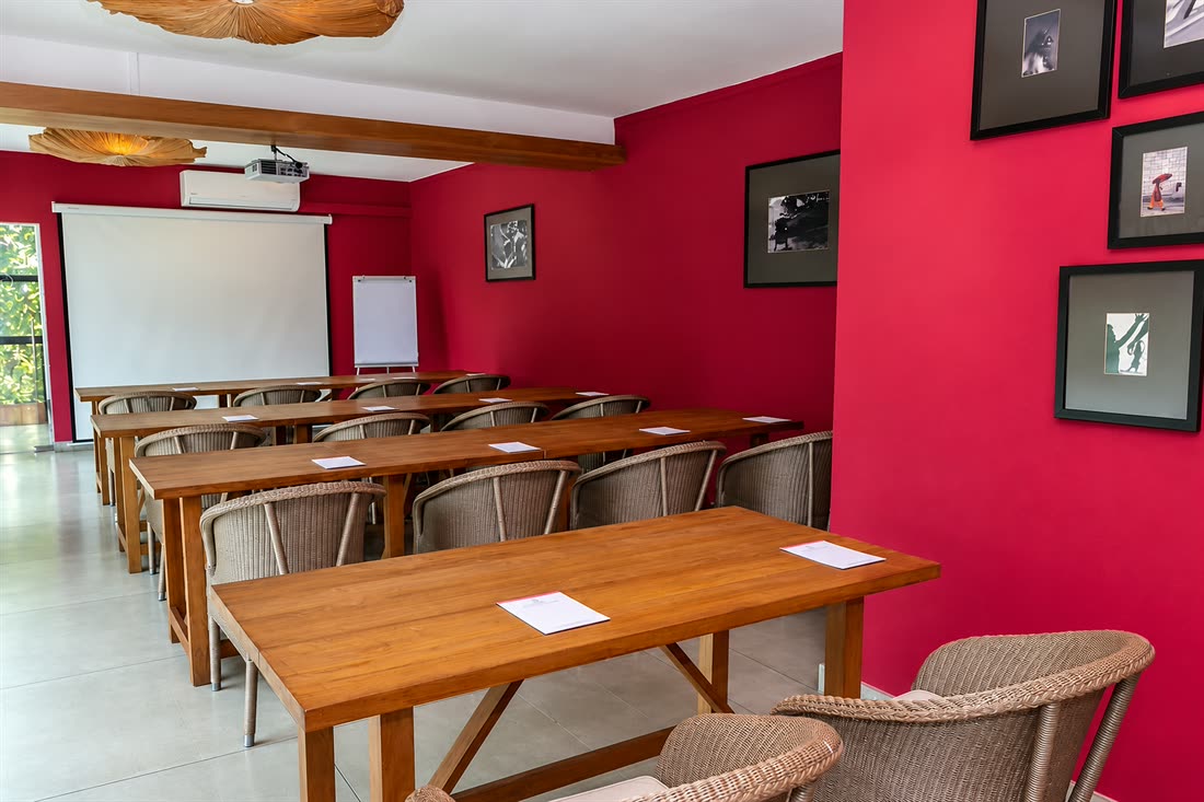 The Scarlet Room set classroom-style, rows of timber tables and cane chairs facing the screen.