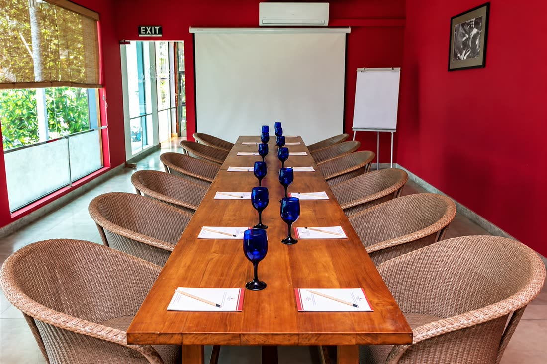 The Scarlet Room set for a meeting, one long timber table with notepads at every seat under the red wall and the projector screen.