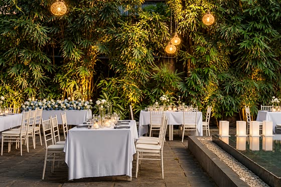 A reception laid in the garden at Colombo Court, round tables in white under lights strung through the trees.