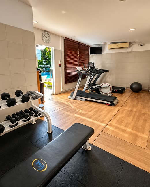 The gym at Colombo Court, a rack of dumbbells and a bench with the treadmill and the pool through the window.
