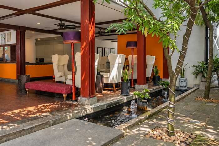 The lobby at Colombo Court, winged armchairs and a daybed under timber beams, a tree and a koi pond in the private courtyard beside it.