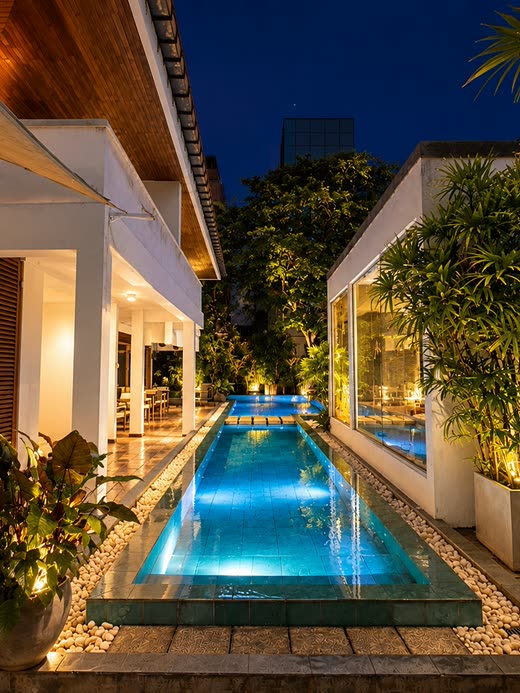 The pool at Colombo Court lit blue at night between the white walls of the garden.