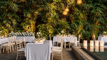 A reception laid in the garden at Colombo Court, round tables in white under lights strung through the trees.
