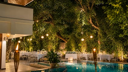 The poolside garden at Colombo Court after dark, lanterns in the trees and tables laid beside the lit pool.