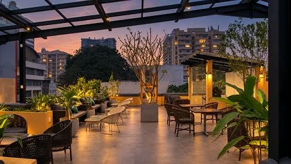 The rooftop at Cloud Caf&eacute; & Bar at twilight, lit trees in planters and cane chairs under the glass roof.