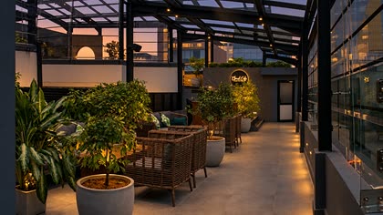 Low cane seating along the rooftop at Cloud Caf&eacute; & Bar, plants in white pots and warm light along the floor.