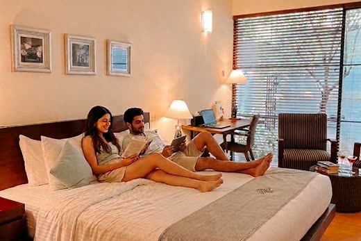 A couple resting on the bed in a room at Colombo Court, bags set down and the garden through the window.