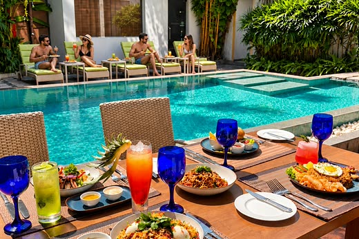 Lunch and cold drinks on a table at the edge of the pool at Amber Poolside, loungers under the trees beyond.