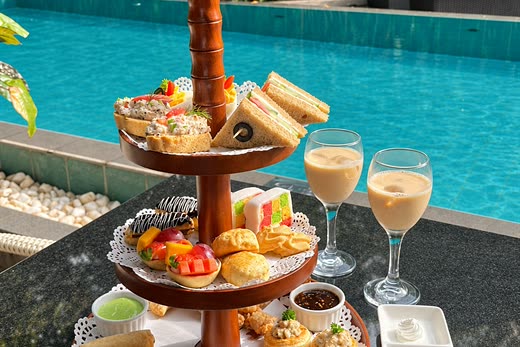 A three-tier afternoon tea stand beside the turquoise pool at Amber Poolside, two glasses of iced tea alongside.